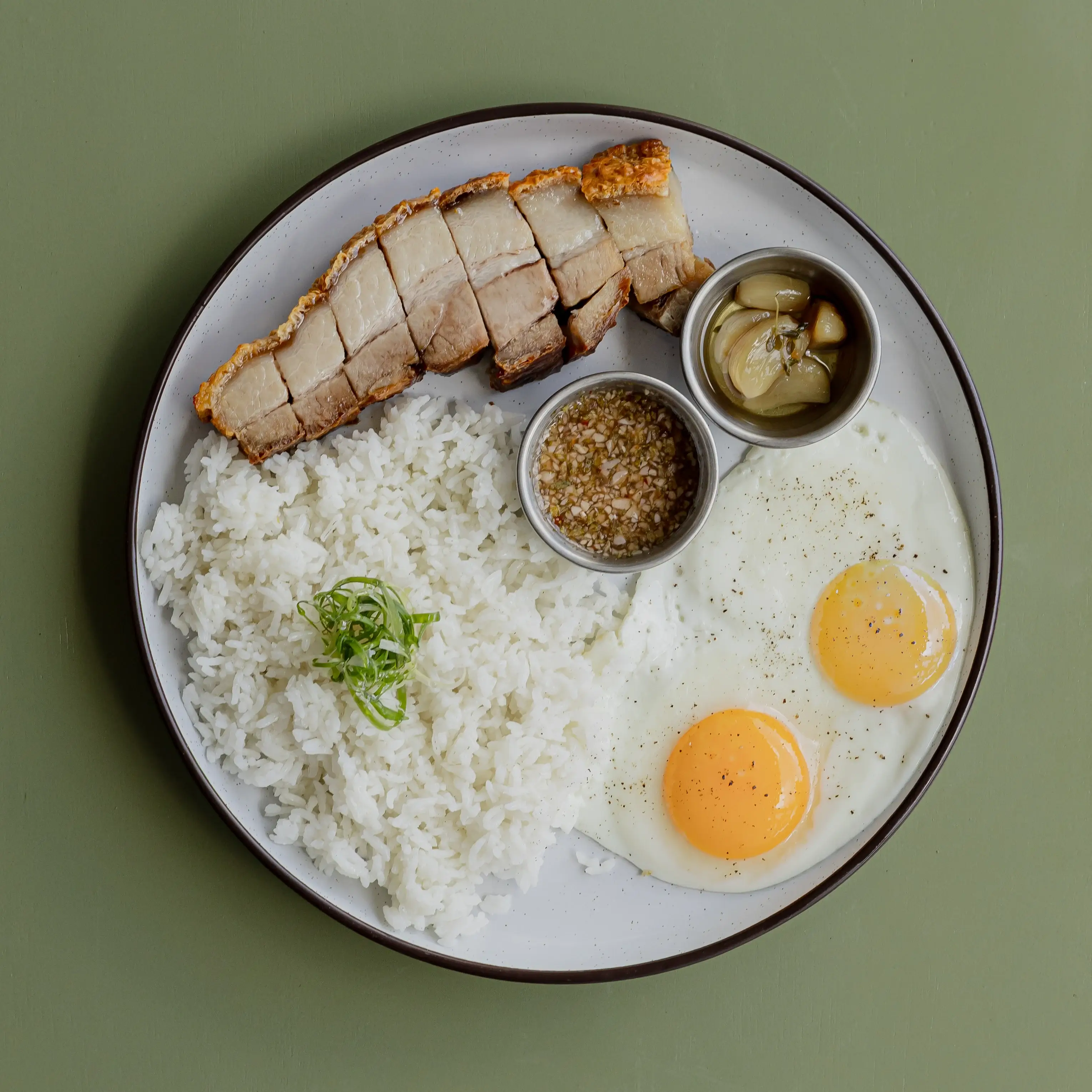 Crispy Pork belly on rice, two sunny side up eggs, garlic confit, crack sauce